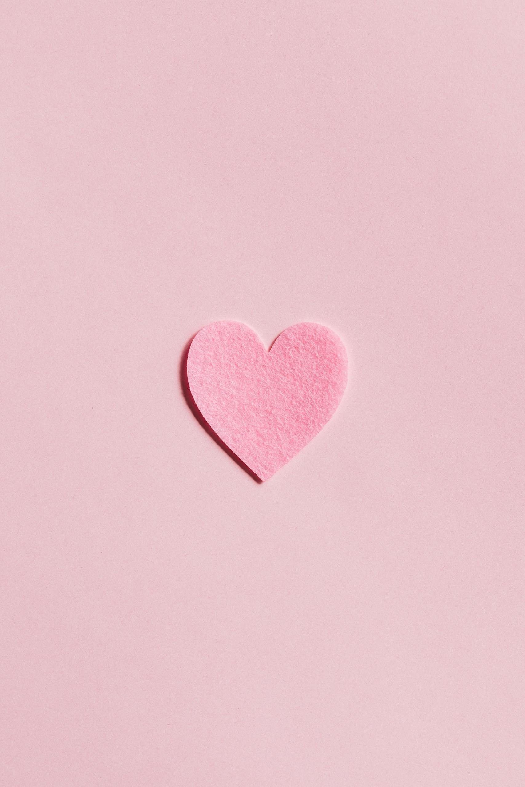 A simple pink felt heart on a light pink background, perfect for Valentine's Day themes.