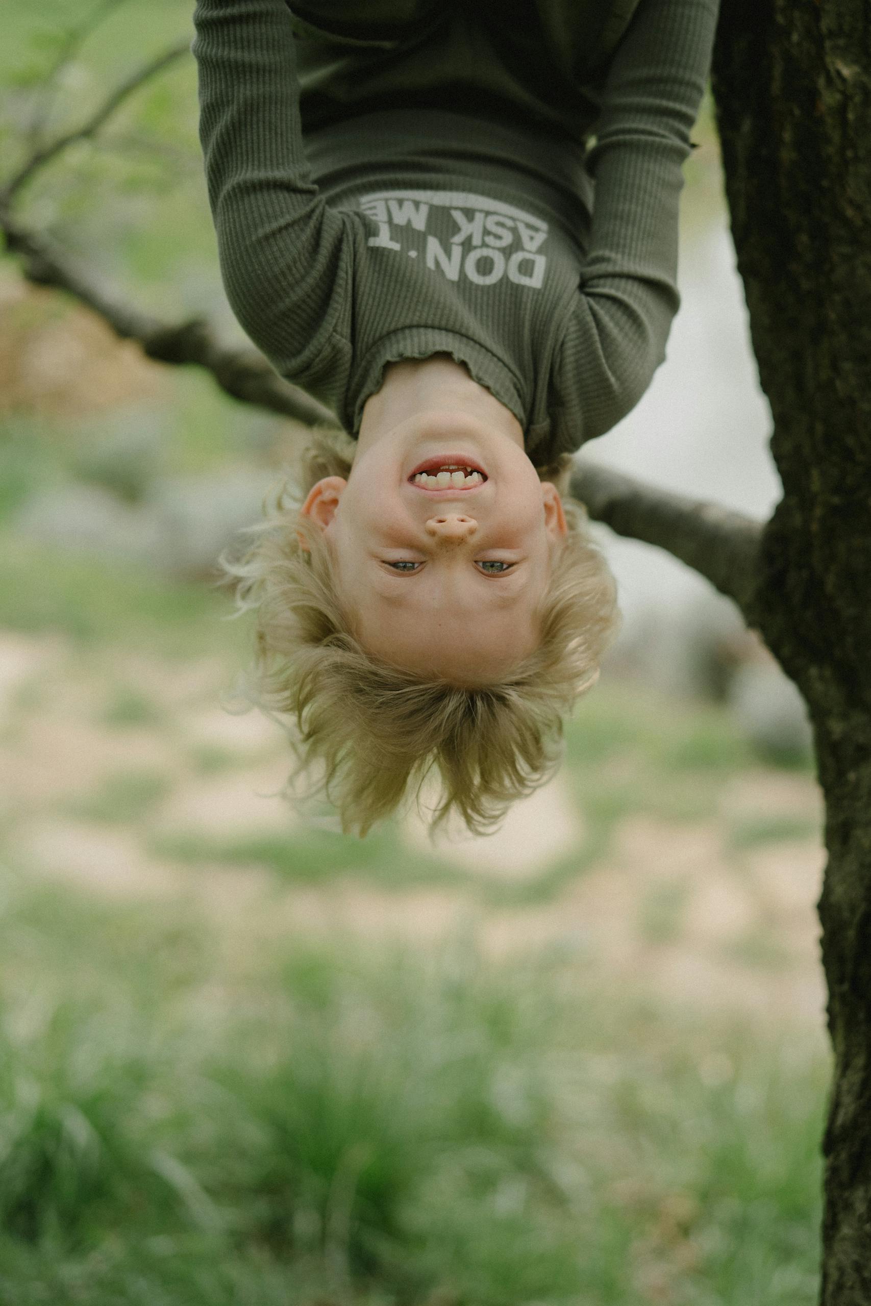 Playful child hanging upside down from a tree, enjoying a fun day outdoors.